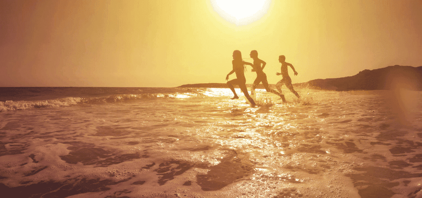 Three people running joyfully in the shallow waves at sunset, with a glowing golden sky reflecting on the ocean. Perfect for EasyJet Holidays travel inspiration.