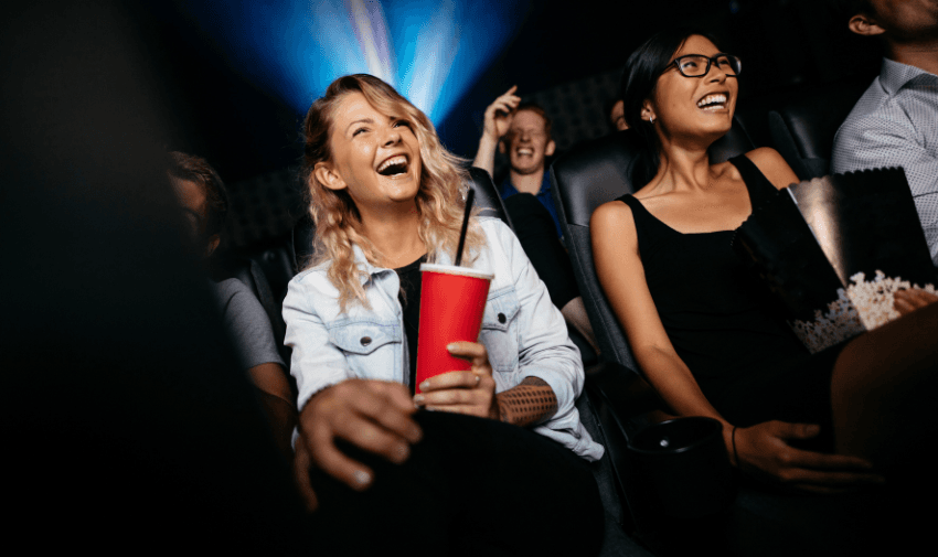 People wearing 3D glasses enjoying a movie in a cinema, seated in red chairs with popcorn and drinks on their laps, under a spotlight from the projector – perfect for showcasing cinema discounts for disabled people.