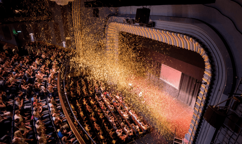 Packed theatre auditorium with an arched stage and golden confetti raining down during a live performance, highlighting exciting entertainment experiences and accessible theatre discounts for disabled people across the UK.