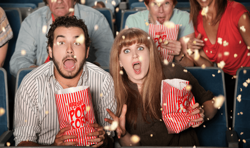 People in a cinema reacting with wide-eyed excitement as popcorn flies through the air during a dramatic movie moment. Great visual for showcasing accessible cinema discounts for disabled people and inclusive film deals for carers.
