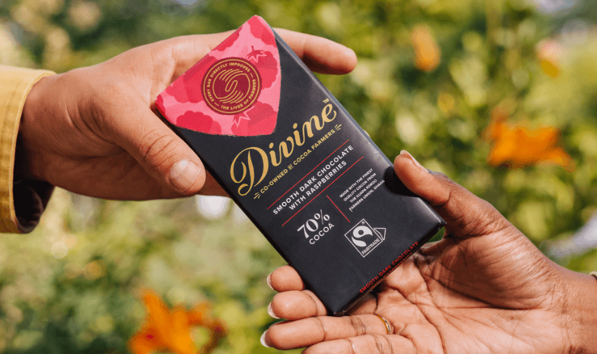 Two hands exchanging a Divine Smooth Dark Chocolate with Raspberries 70% Cocoa bar outdoors, ideal for ethical gift giving and Fairtrade chocolate offers for disabled shoppers in the UK.
