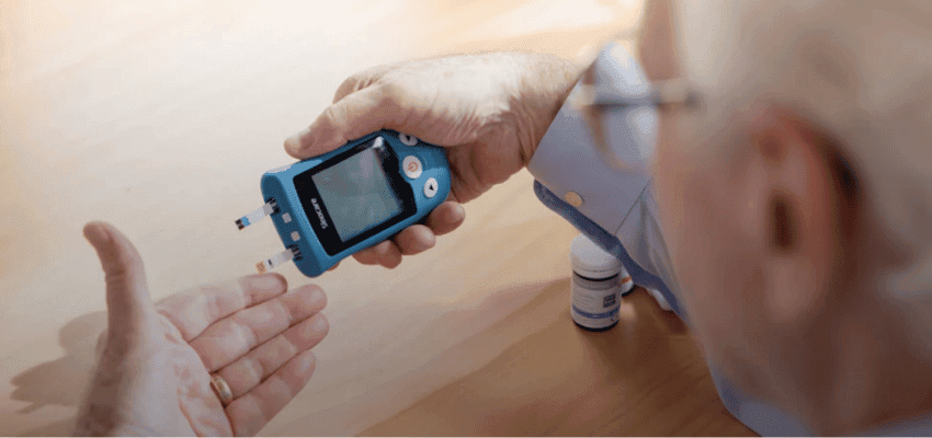 Older man using a Sinocare blood glucose meter at home, diabetes monitoring.