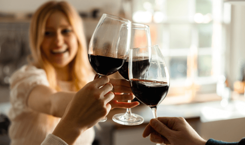 Three people clinking red wine glasses in a bright kitchen setting, celebrating with smiles and natural light, symbolising sociable wine moments and accessible lifestyle discounts for disabled people across the UK.