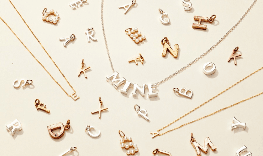 Flatlay of customisable alphabet charms in gold, silver and rose gold tones from Posh Totty, including a silver necklace with MINE spelled out, ideal for personalised jewellery gifts. Jewellery Discounts for Disabled Adults.