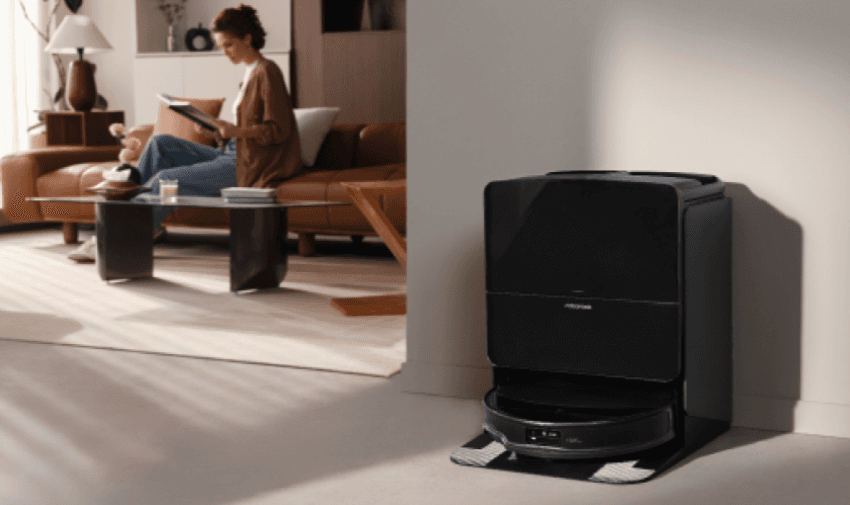 A stylish black Roborock vacuum cleaner in its dock inside a modern living room while a woman reads in the background, showing hands-free cleaning. Useful for disabled home maintenance discounts and accessible tech savings in the UK.