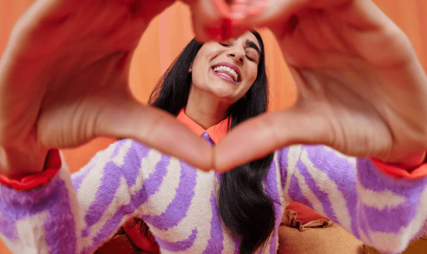 Smiling woman creating a heart shape with her hands in a joyful pose, representing feel-good gift ideas and personalised presents from Not On The High Street UK