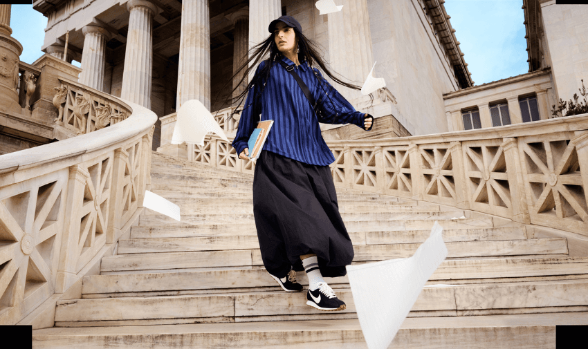 Woman wearing Nike trainers and sporty streetwear walking down grand marble steps with wind-blown papers, promoting fashion and footwear discounts for disabled students and carers.