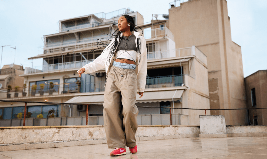 Young woman dancing in pink Nike trainers and relaxed loungewear on a rooftop, showcasing inclusive fashion with mobility discounts and disabled student offers