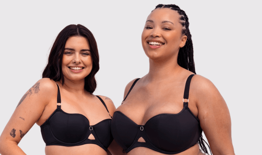 Two smiling women wearing matching black bras, standing side by side against a light grey background. Inclusive lingerie discounts UK, adaptive underwear deals for disabled people, accessible fashion offers.