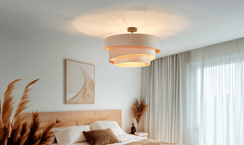 Modern circular ceiling light with a layered shade design in a minimalist bedroom, softly lighting a natural wood bed with neutral decor, promoting accessible lighting products and smart home savings for disabled people across the UK.