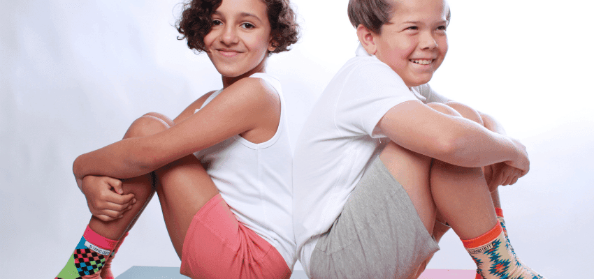 Two smiling children sitting back-to-back wearing vibrant and colourful socks, promoting Intots's inclusive designs. Highlighting Purpl's exclusive disabled discounts, making accessible fashion and adaptive clothing affordable for families in the UK.