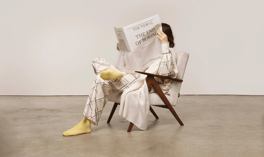 Woman reading ‘The End of Boring’ newspaper while lounging in Tonic pyjamas – stylish adaptive hospital and recovered clothing.