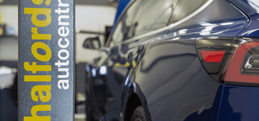 A close-up view of a car parked inside a Halfords Autocentre next to a branded service pillar, promoting vehicle care savings through Purpl discounts for people with disabilities and long term health conditions.