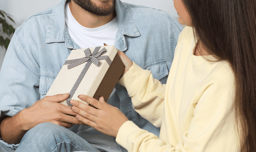 A couple exchanges a neatly wrapped gift with a black-and-white ribbon, representing thoughtful gifting. Useful for Disability-Friendly Gift Ideas and Everyday Gift Discounts for Disabled People.