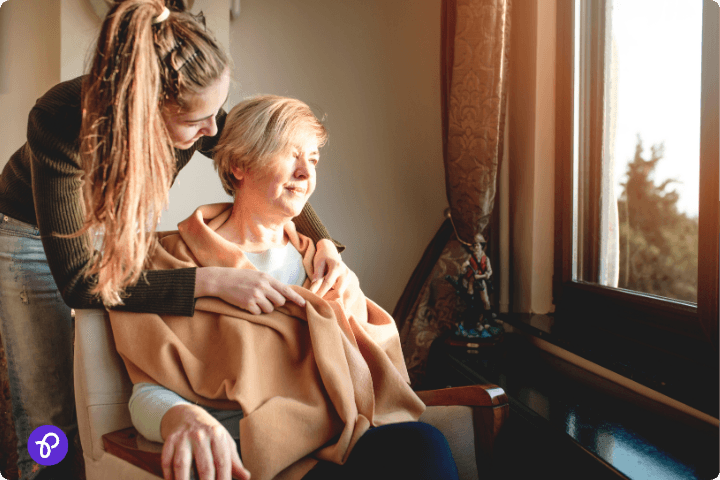 Scope disability energy community support. A young woman comforting an elderly lady by the window, illustrating community support for disabilities.