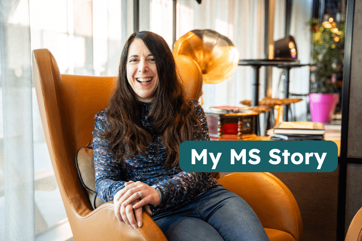 Woman with long brown hair smiling while seated in a cosy armchair, sharing her MS journey – inspiring stories supporting disabled community awareness and Purpl shopping discounts for disabled people.